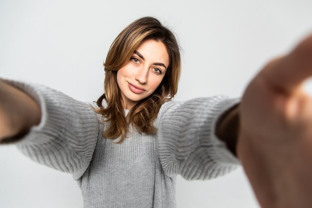 Ritratto di giovane donna attraente che fa la foto del selfie sullo smartphone isolata su una parete grigia