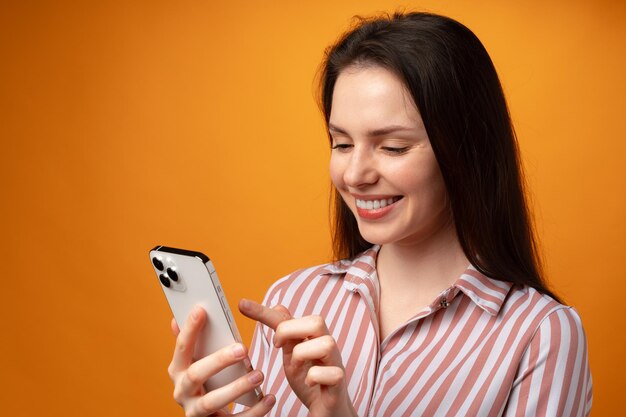 Ritratto di giovane donna attraente che usa il suo smartphone su sfondo giallo