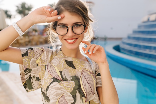 Ritratto di giovane donna, bella ragazza vicino alla bella piscina, spa hotel, resort. Divertirsi, godersi le vacanze, le vacanze. Indossare occhiali alla moda, t-shirt, manicure a filo corto, orologi.