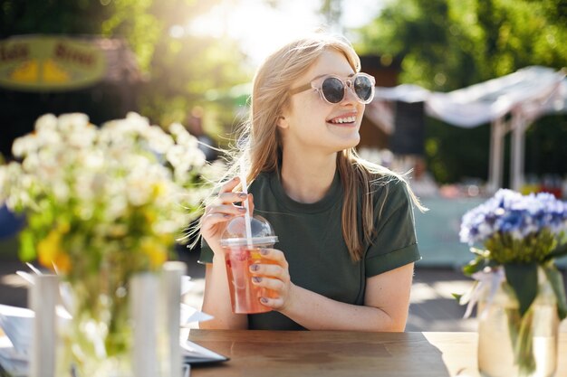 Ritratto di giovane donna blogger alimentare che beve limonata con gli occhiali e sorridente.