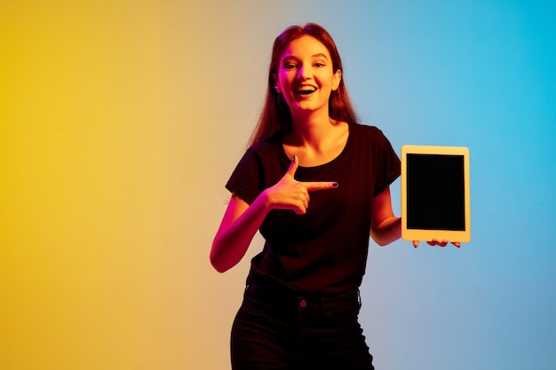 Ritratto di giovane donna caucasica su sfondo blu-giallo sfumato per studio in luce al neon. Concetto di gioventù, emozioni umane, espressione facciale, vendite, annuncio. Bellissima modella bruna.