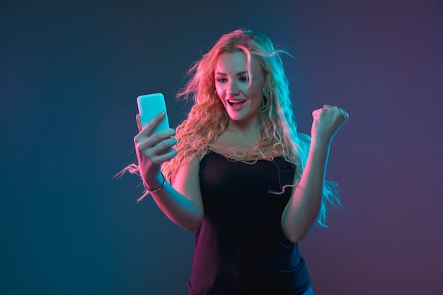 Ritratto di giovane donna caucasica su sfondo sfumato in luce al neon. Bellissimo modello femminile con un aspetto insolito. Concetto di emozioni umane, espressione facciale, vendite, annuncio. Fare selfie, scommesse, acquisti.