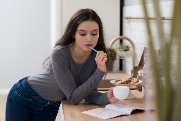 Ritratto di giovane donna che fa i compiti mentre si mangia il caffè