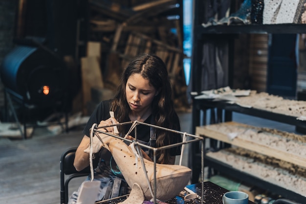 Ritratto di giovane donna che gode del lavoro preferito in officina. Il vasaio lavora con cura sulla balena d'argilla