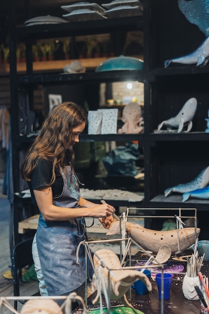 Ritratto di giovane donna che gode del lavoro preferito in officina. Il vasaio lavora con cura sulla balena d'argilla