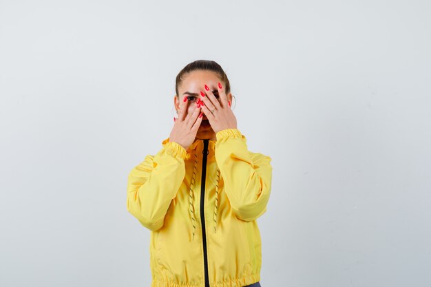 Ritratto di giovane donna che guarda attraverso le dita in giacca gialla e sembra una vista frontale positiva