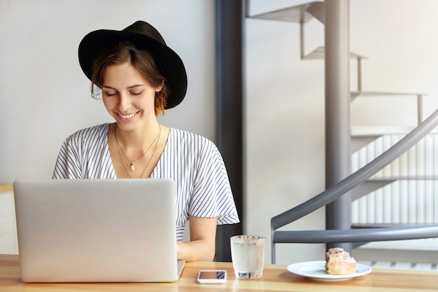 Ritratto di giovane donna che indossa un grande cappello e utilizzando laptop