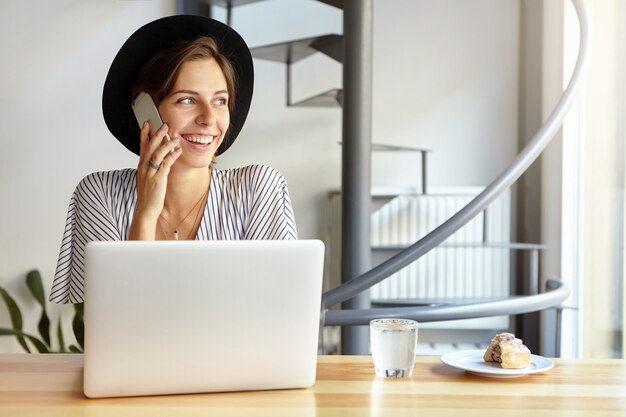 Ritratto di giovane donna che indossa un grande cappello e utilizzando laptop