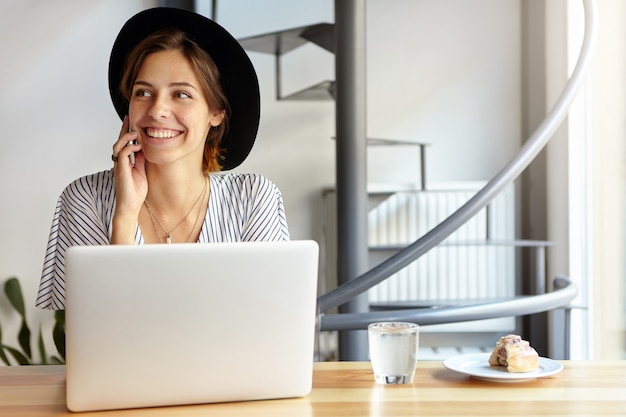 Ritratto di giovane donna che indossa un grande cappello e utilizzando laptop