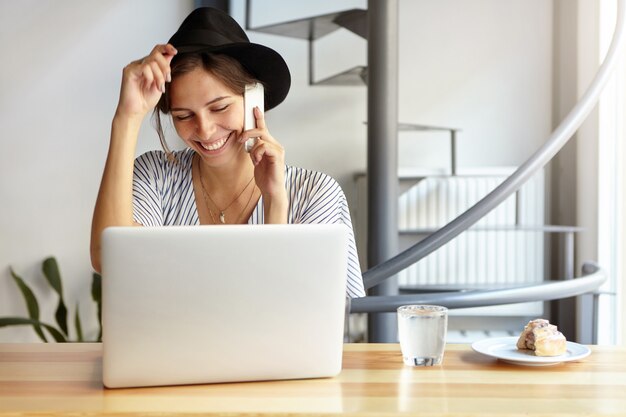 Ritratto di giovane donna che indossa un grande cappello e utilizzando laptop