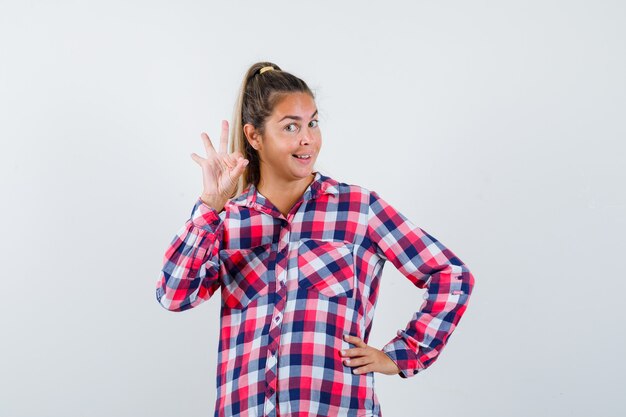 Ritratto di giovane donna che mostra il gesto giusto in camicia controllata e guardando felice vista frontale