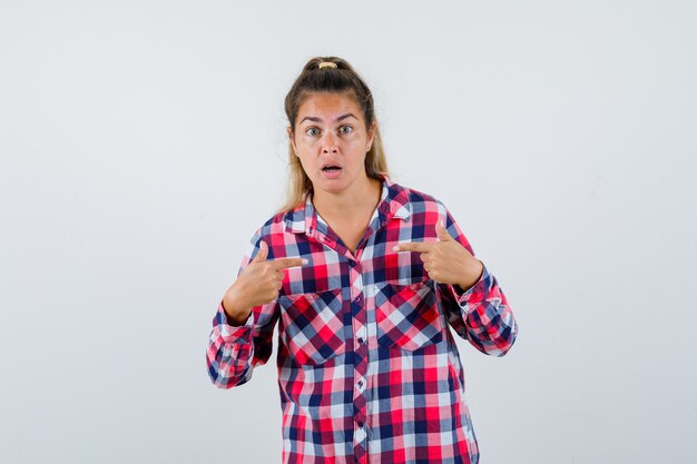 Ritratto di giovane donna che punta a se stessa in camicia a quadri e guardando perplesso vista frontale