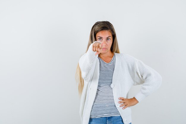 Ritratto di giovane donna che punta alla telecamera in t-shirt, giacca e guardando curioso vista frontale