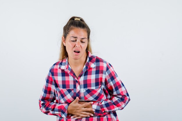 Ritratto di giovane donna che soffre di mal di stomaco in camicia a quadri e guardando malessere vista frontale