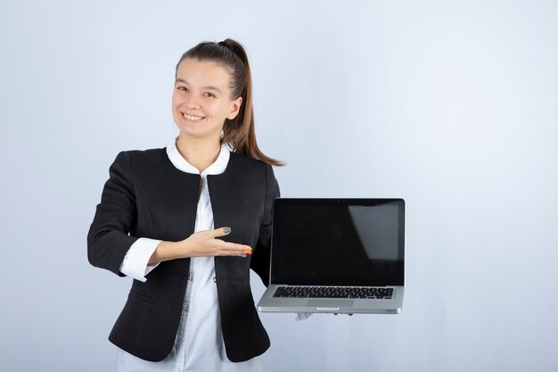 Ritratto di giovane donna che tiene il computer portatile sul muro bianco.