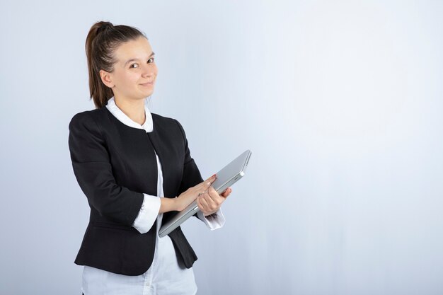 Ritratto di giovane donna che tiene il computer portatile sul muro bianco.