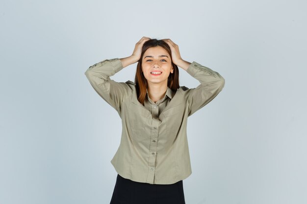 Ritratto di giovane donna che tiene le mani sulla testa in camicia, gonna e sembra felice vista frontale