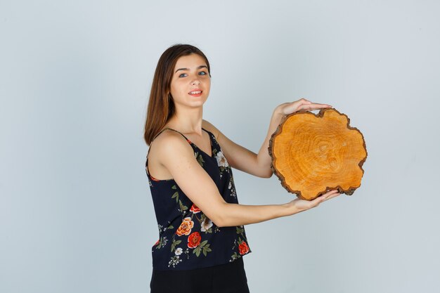 Ritratto di giovane donna che tiene un pezzo di legno in camicetta, gonna e sembra allegra vista frontale