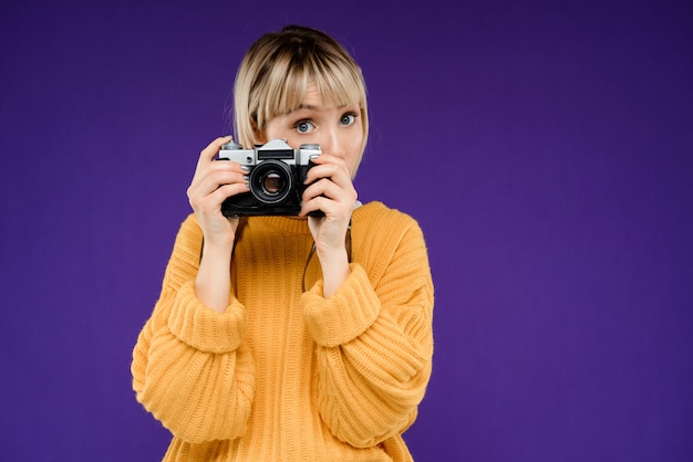 Ritratto di giovane donna con la macchina fotografica sopra la parete viola