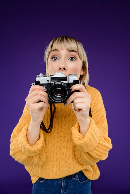 Ritratto di giovane donna con la macchina fotografica sopra la parete viola