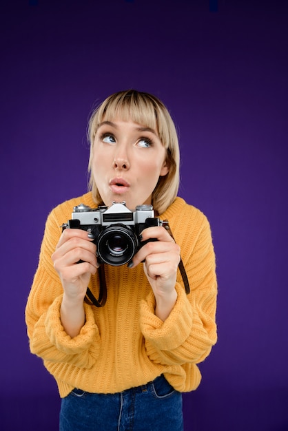 Ritratto di giovane donna con la macchina fotografica sopra la parete viola