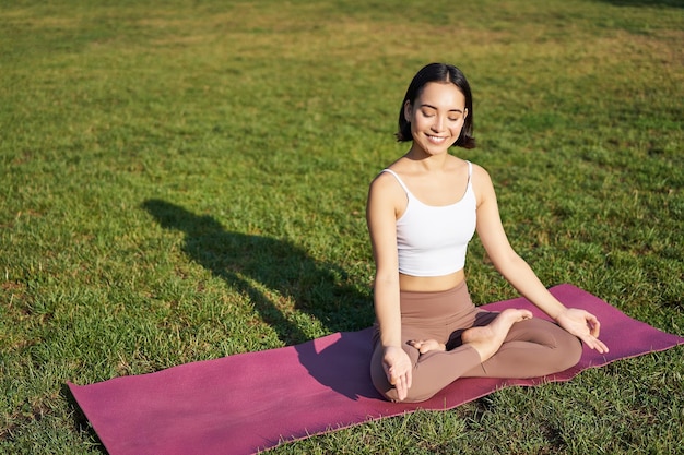Ritratto di giovane donna consapevole pratica yoga esercitando inspirare ed espirare all'aria aperta nel parco sitt