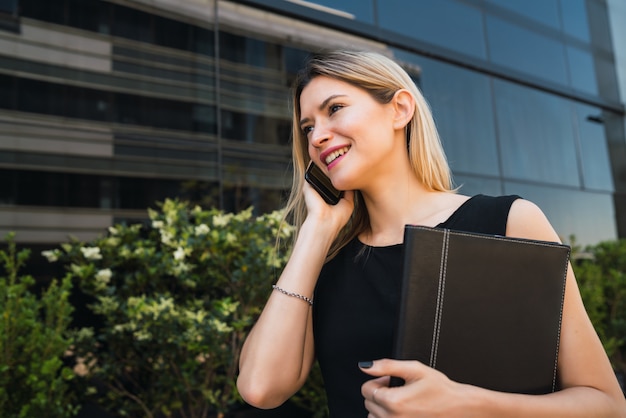 Ritratto di giovane donna d'affari parlando al telefono mentre in piedi all'aperto in strada. Concetto di affari.