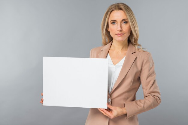 Ritratto di giovane donna di affari che mostra cartello bianco in bianco su sfondo grigio