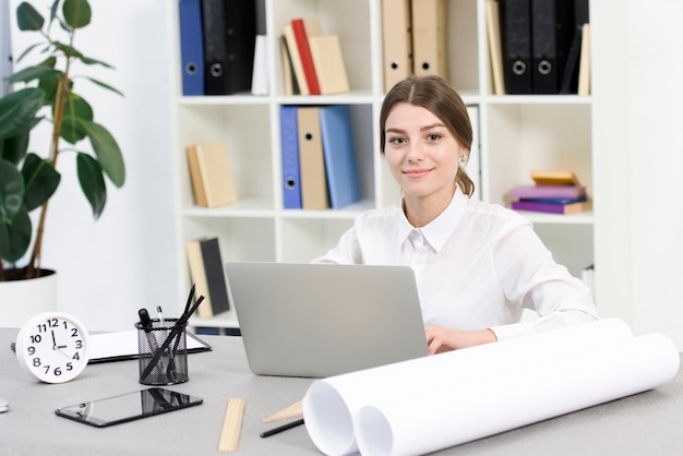 Ritratto di giovane donna di affari sorridente che utilizza computer portatile nell&#39;ufficio