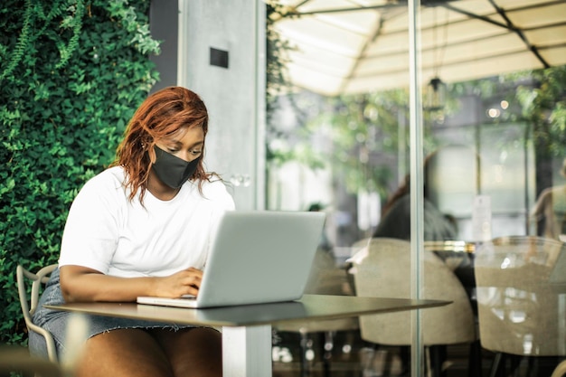 ritratto di giovane donna di colore che utilizza un computer con maschera