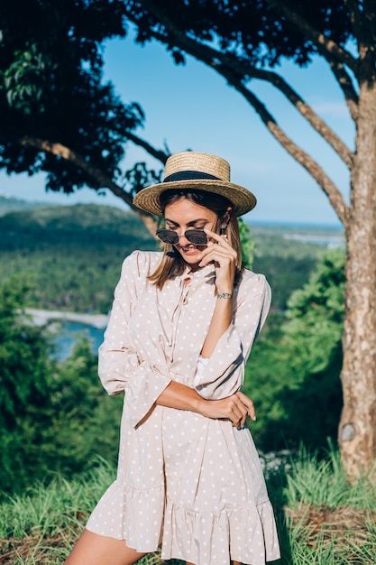 Ritratto di giovane donna felice in abito estivo, occhiali da sole e cappello di paglia