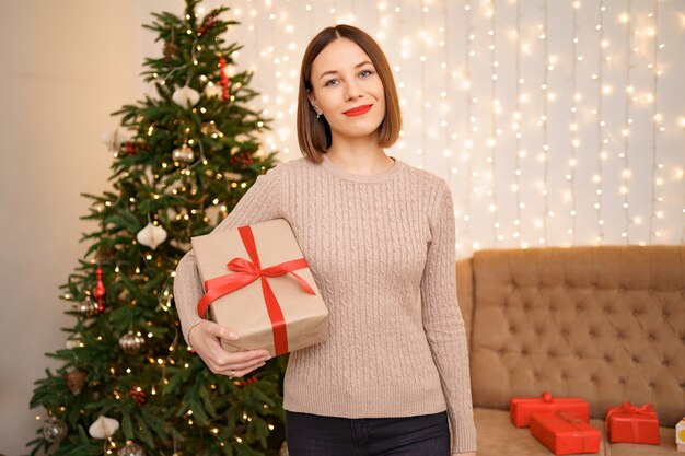 Ritratto di giovane donna felice labbra rosse che guarda l'obbiettivo che tiene una confezione regalo avvolta