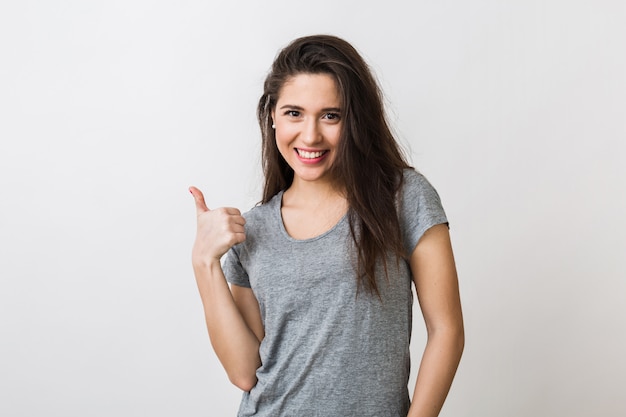 Ritratto di giovane donna graziosa alla moda sorridente in maglietta grigia su, isolato, mostrando il pollice in su, gesto felice e positivo