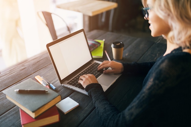 Ritratto di giovane donna graziosa che si siede al tavolo in camicia nera che lavora al computer portatile in ufficio di co-working