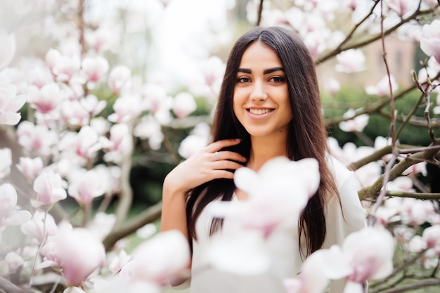 Ritratto di giovane donna graziosa vicino al fiore dell'albero di magnolia in fiore. Tempo di primavera