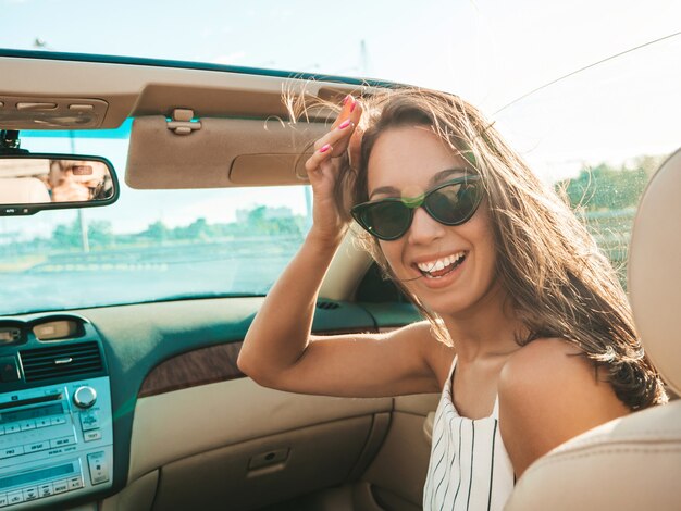 Ritratto di giovane donna hipster bella e sorridente in auto decappottabile