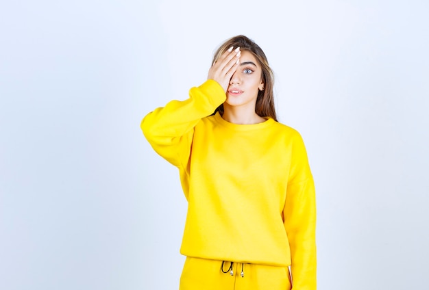 Ritratto di giovane donna in abito giallo in piedi e che si copre gli occhi