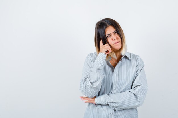 Ritratto di giovane donna in piedi in posa di pensiero in camicia oversize e guardando pensieroso vista frontale