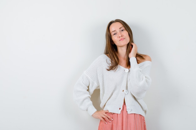 Ritratto di giovane donna in posa mentre si tocca i capelli in cardigan isolato