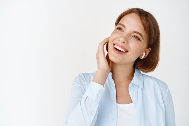 Ritratto di giovane donna naturale che ascolta musica in cuffie wireless sorridendo e guardando da parte Ragazza che gode di una canzone sonora in cuffie su sfondo bianco