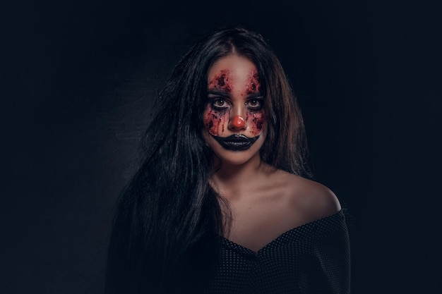 Ritratto di giovane donna nel ruolo di malvagio clown spaventoso in studio fotografico scuro.