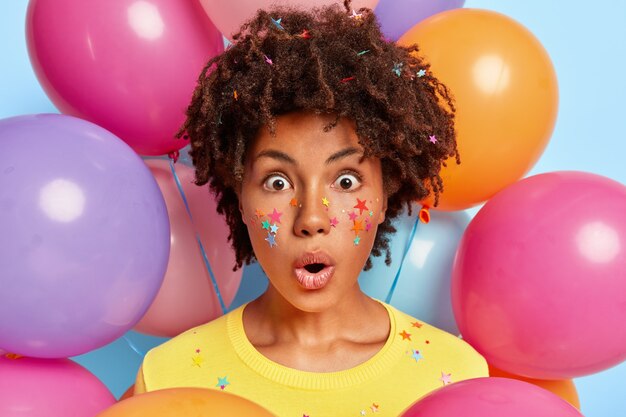 Ritratto di giovane donna spaventata in posa circondata da palloncini colorati compleanno