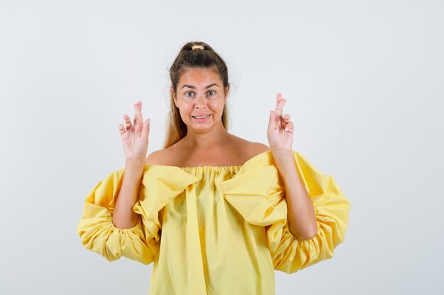 Ritratto di giovane donna tenendo le dita incrociate in abito giallo e guardando speranza vista frontale