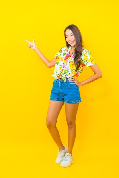 Ritratto di giovane e bella donna asiatica che indossa maglietta colorata e tiro con il dito sul muro giallo