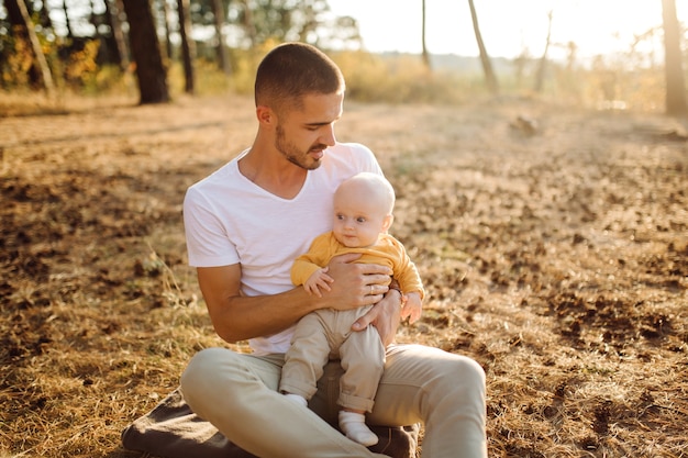 Ritratto di giovane famiglia attraente con figlio piccolo bambino, in posa nella bellissima pineta autunno al giorno pieno di sole. Bell'uomo e la sua bella mora moglie