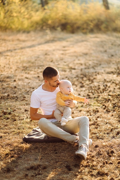 Ritratto di giovane famiglia attraente con figlio piccolo bambino, in posa nella bellissima pineta autunno al giorno pieno di sole. Bell'uomo e la sua bella mora moglie