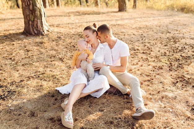 Ritratto di giovane famiglia attraente con figlio piccolo bambino, in posa nella bellissima pineta autunno al giorno pieno di sole. Bell'uomo e la sua bella mora moglie