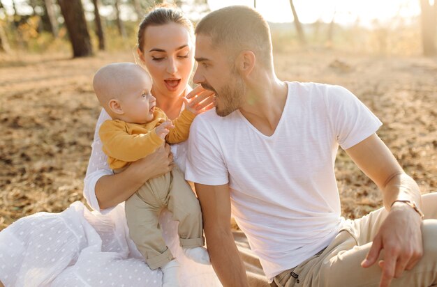 Ritratto di giovane famiglia attraente con figlio piccolo bambino, in posa nella bellissima pineta autunno al giorno pieno di sole. Bell'uomo e la sua bella mora moglie