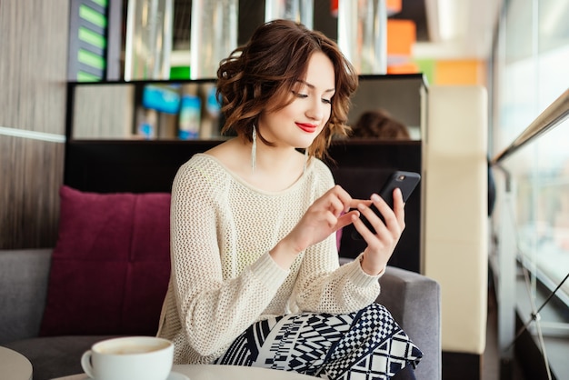 Ritratto di giovane imprenditrice utilizzare il telefono cellulare mentre seduto nella caffetteria confortevole
