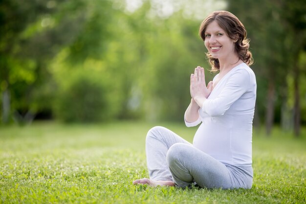 Ritratto di giovane modello incinta meditando sul prato erboso